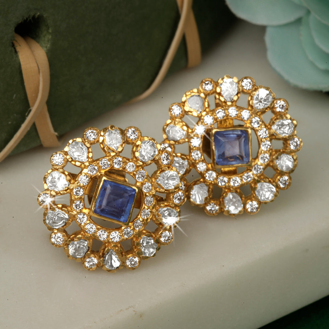 A pair of silver earrings with gold polki design and blue stones.