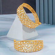 Gold bracelet with intricate design on a white stand against a gray background