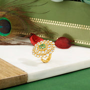 Gold plated silver ring with green gemstone on a white surface with a peacock feather and decorative box in the background.