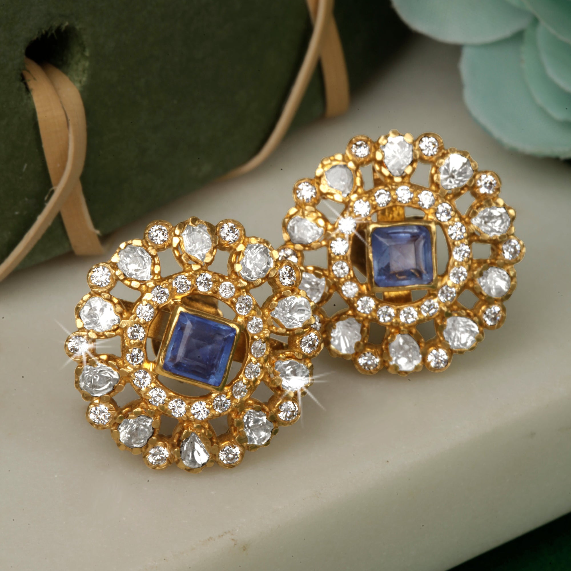 A pair of silver earrings with gold polki design and blue stones.