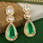 Gold and green teardrop silver earrings on a textured surface with a green background