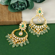 Gold and green silver earrings on a green surface with flowers in the background