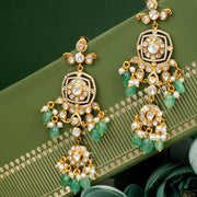 Ornate gold and green silver earrings on a green surface with floral elements.