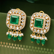 A pair of silver earrings featuring square-shaped moissanite stones with green bead accents and pearl details, displayed against a green floral background.