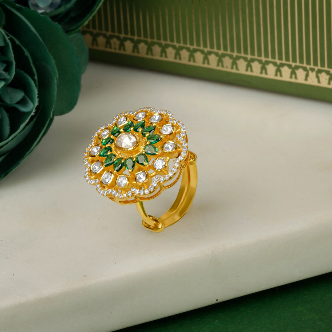 Silver Gold plated ring with green gemstones on a white surface with green flowers and a green box in the background