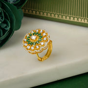 Silver Gold plated ring with green gemstones on a white surface with green flowers and a green box in the background